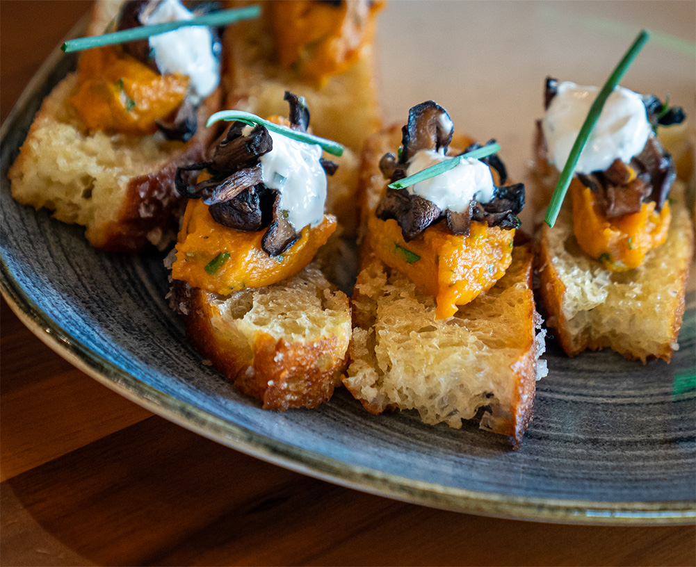 Bread with seasoned squash and truffle mushrooms, served in plate, and topped with fresh chives