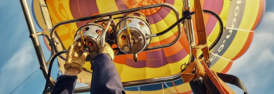 Close-up of a pilot igniting the burner of a colorful hot air balloon against a bright blue sky.