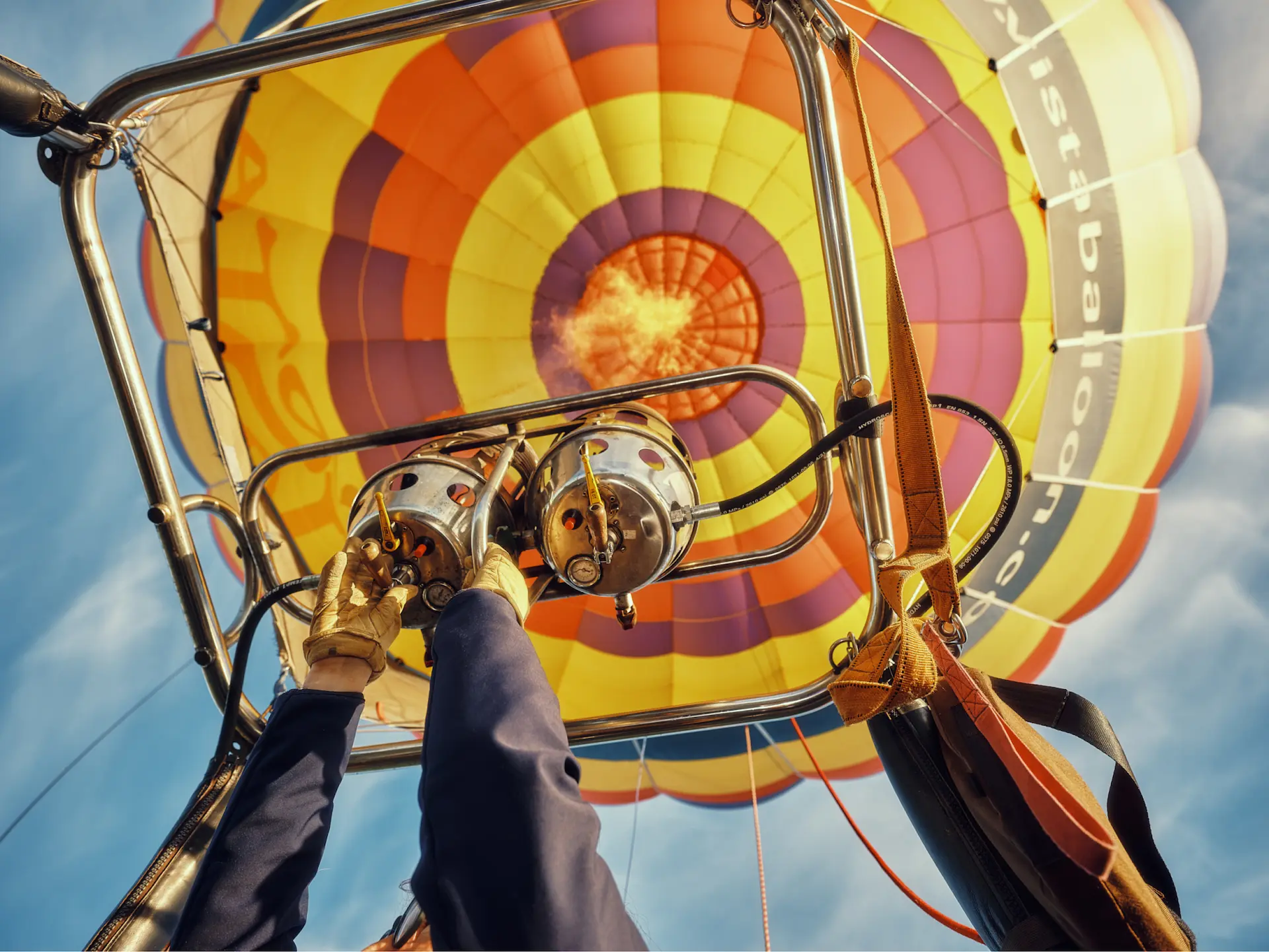Close-up of a pilot igniting the burner of a colorful hot air balloon against a bright blue sky.