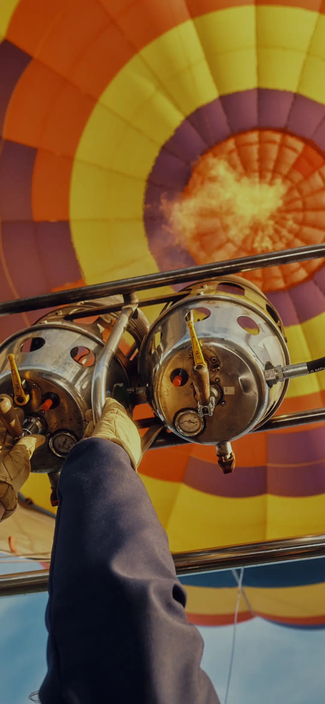 Close-up of a pilot igniting the burner of a colorful hot air balloon against a bright blue sky.