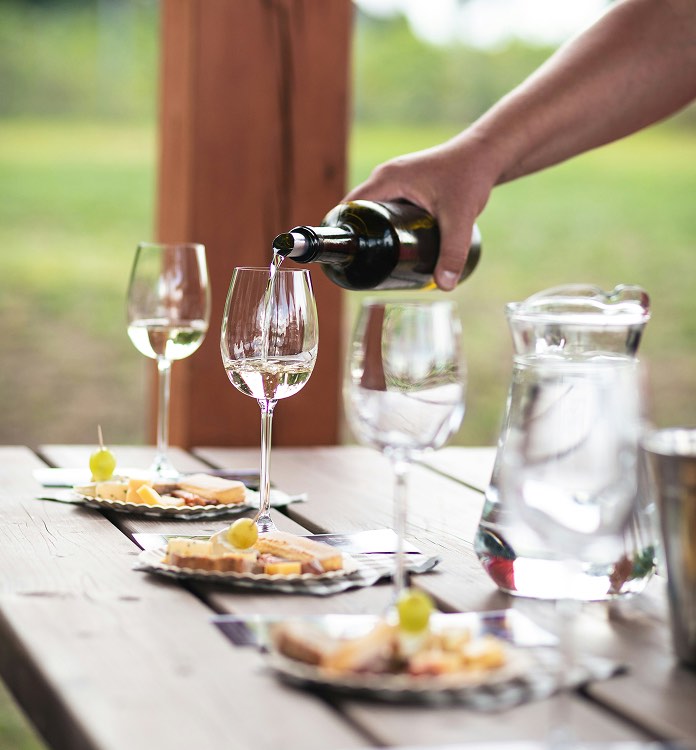 Person pouring wine into a glass next to a plate of appetizers