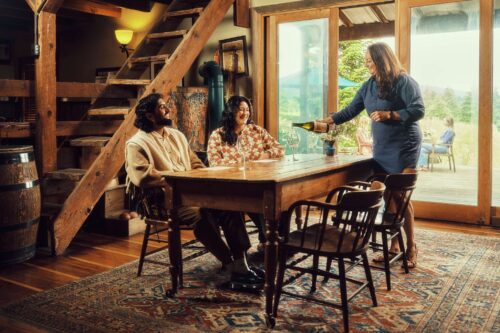 Server pouring wine for two people seated at a table in a rustic setting