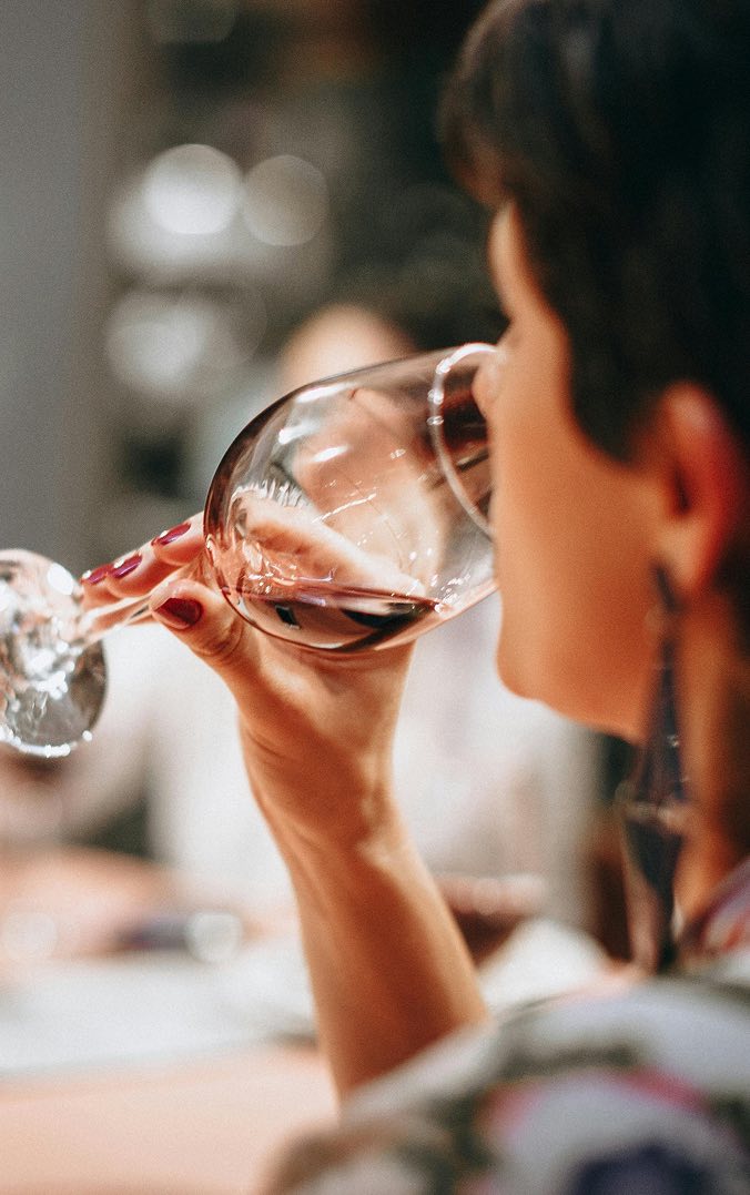 Person sipping wine with friends in background