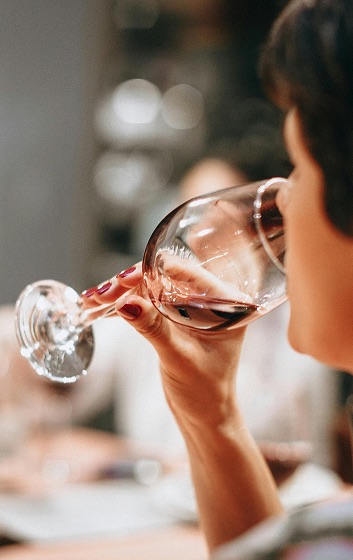 Person sipping wine with friends in background