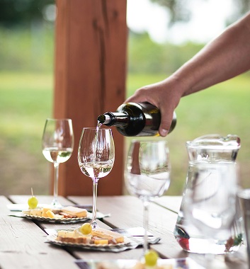Person pouring wine into a glass next to a plate of appetizers