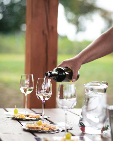 Person pouring wine into a glass next to a plate of appetizers